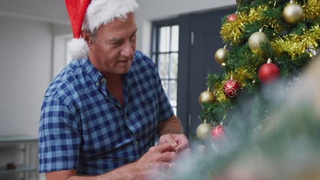 Glücklicher-Kaukasischer-älterer-Mann-Mit-Weihnachtsmütze,-Der-Den-Weihnachtsbaum-Schmückt