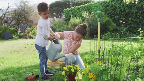 Happy-caucasian-siblings-gardening,-watering-flowers-together
