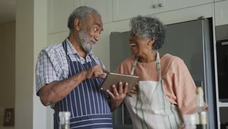 Glückliches-Afroamerikanisches-Seniorenpaar,-Das-Gemeinsam-Kocht-Und-Dabei-Ein-Tablet-Verwendet