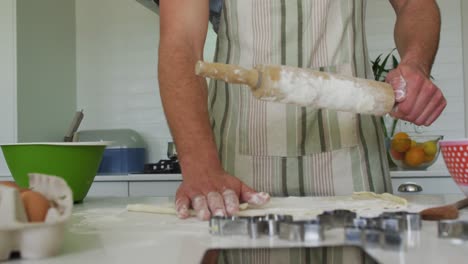 Midsection-of-caucasian-man-rolling-dough-for-baking-in-kitchen