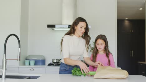 Happy-caucasian-mother-and-daughter-unpacking-groceries-in-kitchen