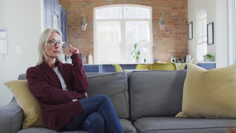 Thoughtful-caucasian-senior-woman-wearing-glasses-sitting-on-the-couch-at-home