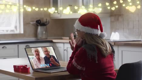 Animation-of-fairy-lights-over-caucasian-woman-in-santa-hat-on-laptop-video-call-at-christmas