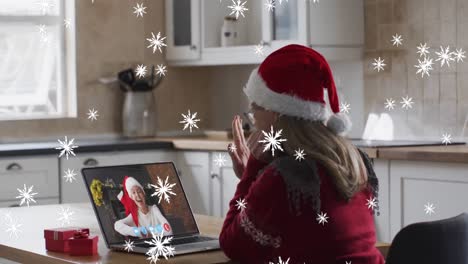 Animation-of-snow-falling-over-caucasian-woman-in-santa-hat-on-laptop-video-call-at-christmas