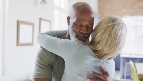 Mixed-race-senior-couple-hugging-each-other-at-home