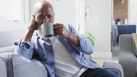 Nachdenklicher-älterer-Afroamerikanischer-Mann-Im-Wohnzimmer,-Der-Auf-Dem-Sofa-Sitzt-Und-Kaffee-Trinkt
