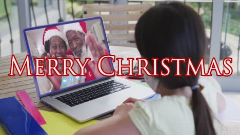 Animation-of-merry-christmas-text-over-girl-with-face-mask-on-laptop-video-call-with-family