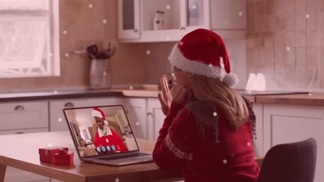 Animation-Von-Weihnachtsschnee,-Der-über-Eine-Frau-Mit-Weihnachtsmütze-Auf-Einem-Laptop-Fällt,-Videoanruf-Mit-Der-Familie