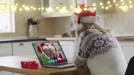 Lichterketten-über-Einer-Kaukasischen-Frau-Mit-Weihnachtsmütze,-Die-Zu-Hause-Einen-Videoanruf-Auf-Dem-Laptop-Führt