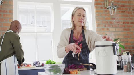 Caucasian-senior-woman-wearing-apron-putting-vegetable-peelings-in-a-compost-bin-in-the-kitchen