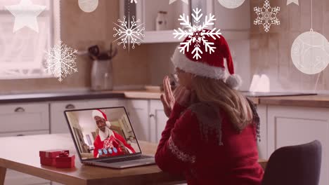 Animation-of-christmas-snowflakes-over-woman-in-santa-hat-on-laptop-video-call-with-family