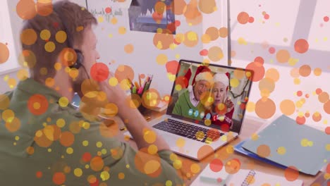 Animation-of-light-spots-over-caucasian-man-on-laptop-video-call-with-family-at-christmas