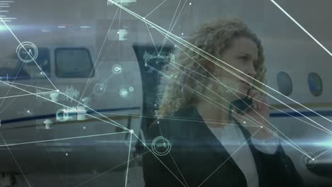 Animation-of-networks-of-connections-over-caucasian-businesswoman-talking-on-smartphone-at-airport