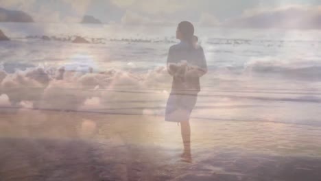 Animation-of-clouds-over-caucasian-woman-walking-on-beach