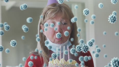 Animation-of-covid-19-virus-cells-over-caucasian-senior-woman-wearing-face-mask-celebrating-birthday
