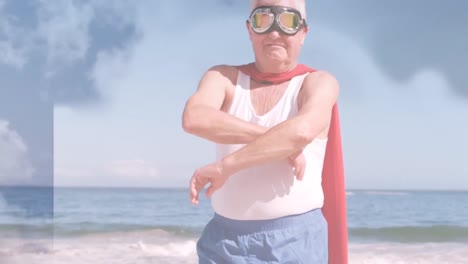 Animation-of-clouds-over-senior-caucasian-man-wearing-superhero-costume-on-beach
