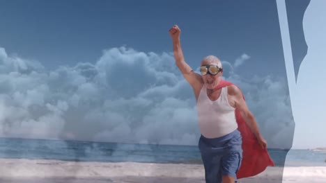 Animation-of-clouds-over-senior-caucasian-man-wearing-superhero-costume-on-beach