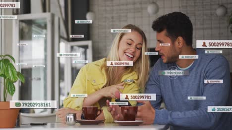 Animation-of-social-media-icons-floating-over-happy-caucasian-couple-using-smartphone-having-coffee