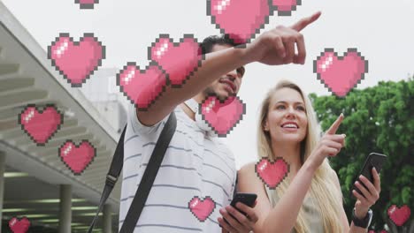 Animation-of-heart-icons-floating-over-happy-caucasian-couple-talking-and-using-smartphone