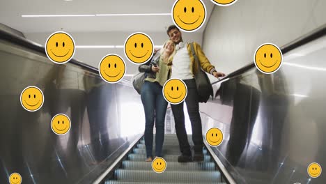 Animation-of-digital-emoji-icons-floating-over-happy-caucasian-couple-embracing-on-moving-stairs