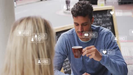 Animation-of-social-media-icons-floating-over-caucasian-couple-talking-and-drinking-coffee