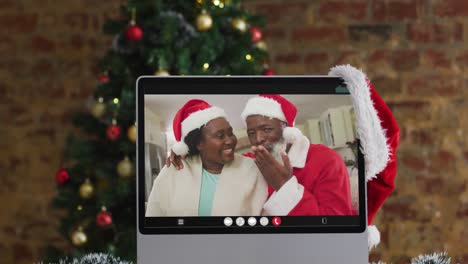 Pareja-De-Ancianos-Afroamericanos-Con-Sombreros-De-Santa-En-Videollamada-En-Computadora,-Con-árbol-De-Navidad