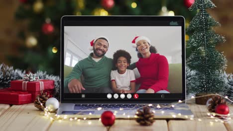 Happy-family-wearing-santa-hats-on-laptop-video-call,-with-christmas-decorations-and-tree