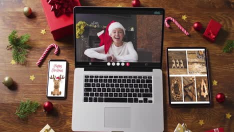 Kaukasische-Frau-Mit-Weihnachtsmütze-Bei-Videoanruf-Auf-Laptop,-Mit-Smartphone,-Tablet-Und-Dekorationen