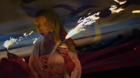 Animation-of-flag-of-columbia-over-woman-dancing-with-sparklers-on-beach
