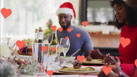 Animation-of-hearts-floating-over-happy-african-american-family-during-dinner-at-christmas