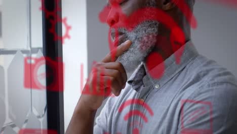 Múltiples-íconos-Digitales-Rojos-Contra-Un-Reflexivo-Hombre-De-Negocios-Afroamericano-En-La-Oficina