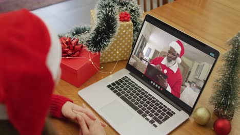 Caucasian-woman-having-christmas-video-call-on-laptop-with-african-american-santa-claus-on-screen