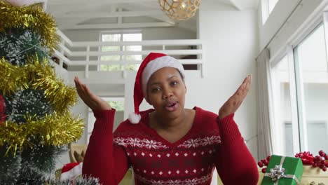 Happy-african-american-plus-size-woman-wearing-santa-claus-hat,-making-video-call-at-christmas