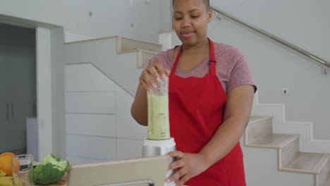 Happy-african-american-plus-size-woman-wearing-apron,-preparing-health-drink-in-kitchen