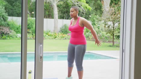 Happy-african-american-plus-size-woman-practicing-yoga,-standing-stretching-next-to-in-garden