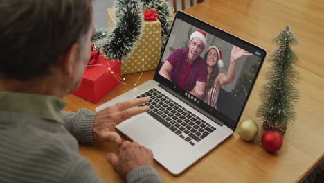 Caucasian-senior-man-having-christmas-video-call-on-laptop-with-caucasian-couple-on-screen