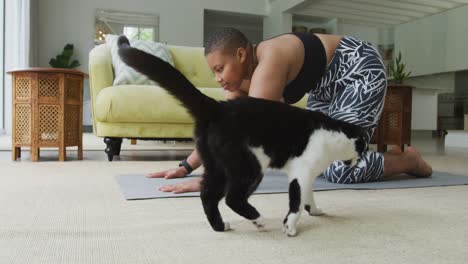 Glückliche-Afroamerikanische-Plus-Size-Frau,-Die-Yoga-Praktiziert-Und-Sich-Im-Wohnzimmer-Mit-Ihrer-Haustierkatze-Dehnt
