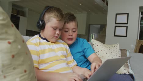 Kaukasischer-Junge-Mit-Seinem-Bruder,-Der-Im-Wohnzimmer-Sitzt-Und-Einen-Laptop-Benutzt