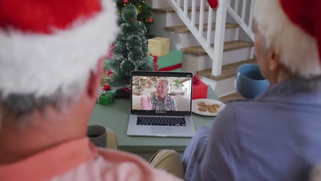 Happy-caucasian-senior-couple-couple-on-video-call-with-male-friend-at-christmas-time