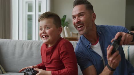 Glücklicher-Kaukasischer-Vater-Mit-Sohn,-Der-Im-Wohnzimmer-Sitzt-Und-Videospiele-Spielt