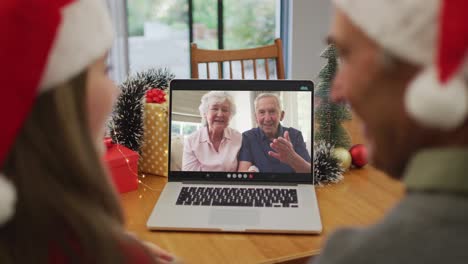 Caucasian-granddaughter-and-grandfather-on-video-call-with-senior-couple-at-christmas-time