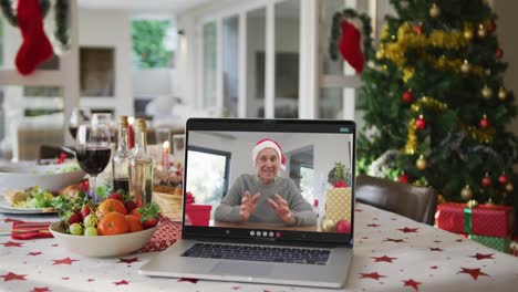 Happy-caucasian-senior-man-in-santa-hat-on-laptop-lying-on-christmas-table