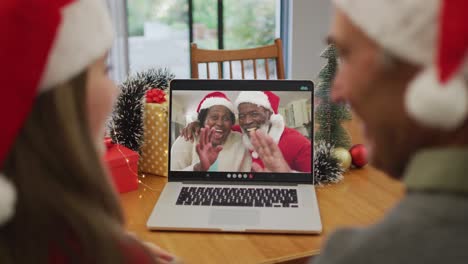 Happy-caucasian-senior-couple-on-video-call-with-senior-couple-at-christmas-time