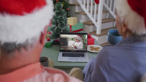 Feliz-Pareja-De-Ancianos-Caucásicos-En-Videollamada-En-Una-Computadora-Portátil-Con-Su-Nieto-Con-Sombrero-De-Santa-En-Navidad