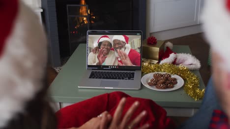 Happy-caucasian-couple-on-video-call-on-laptop-with-senior-couple-at-christmas-time