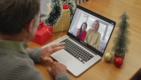 Happy-caucasian-senior-man-on-video-call-with-female-friend-and-her-daughter-at-christmas-time