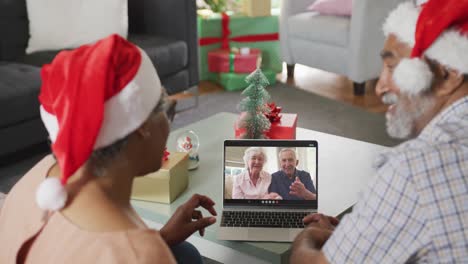Happy-senior-african-american-couple-on-video-call-on-laptop-with-senior-friends-at-christmas-time