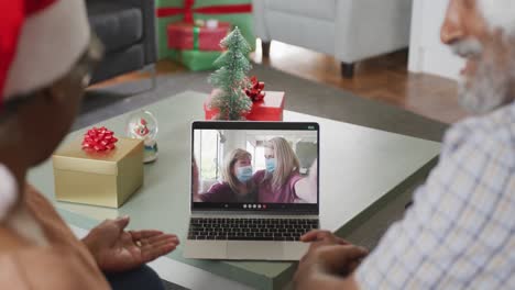 Happy-african-american-senior-couple-on-video-call-with-female-friends-in-face-masks-at-christmas