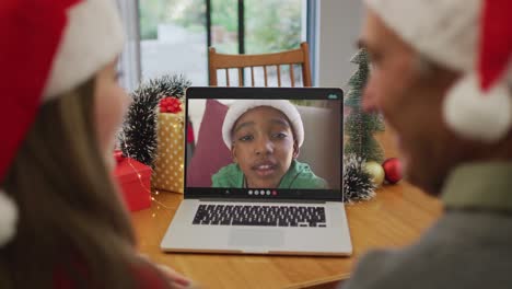 Happy-caucasian-senior-man-and-granddaughter-on-video-call-with-boy-at-christmas-time