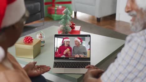 Happy-senior-african-american-couple-on-video-call-with-male-friend-and-daughter-at-christmas